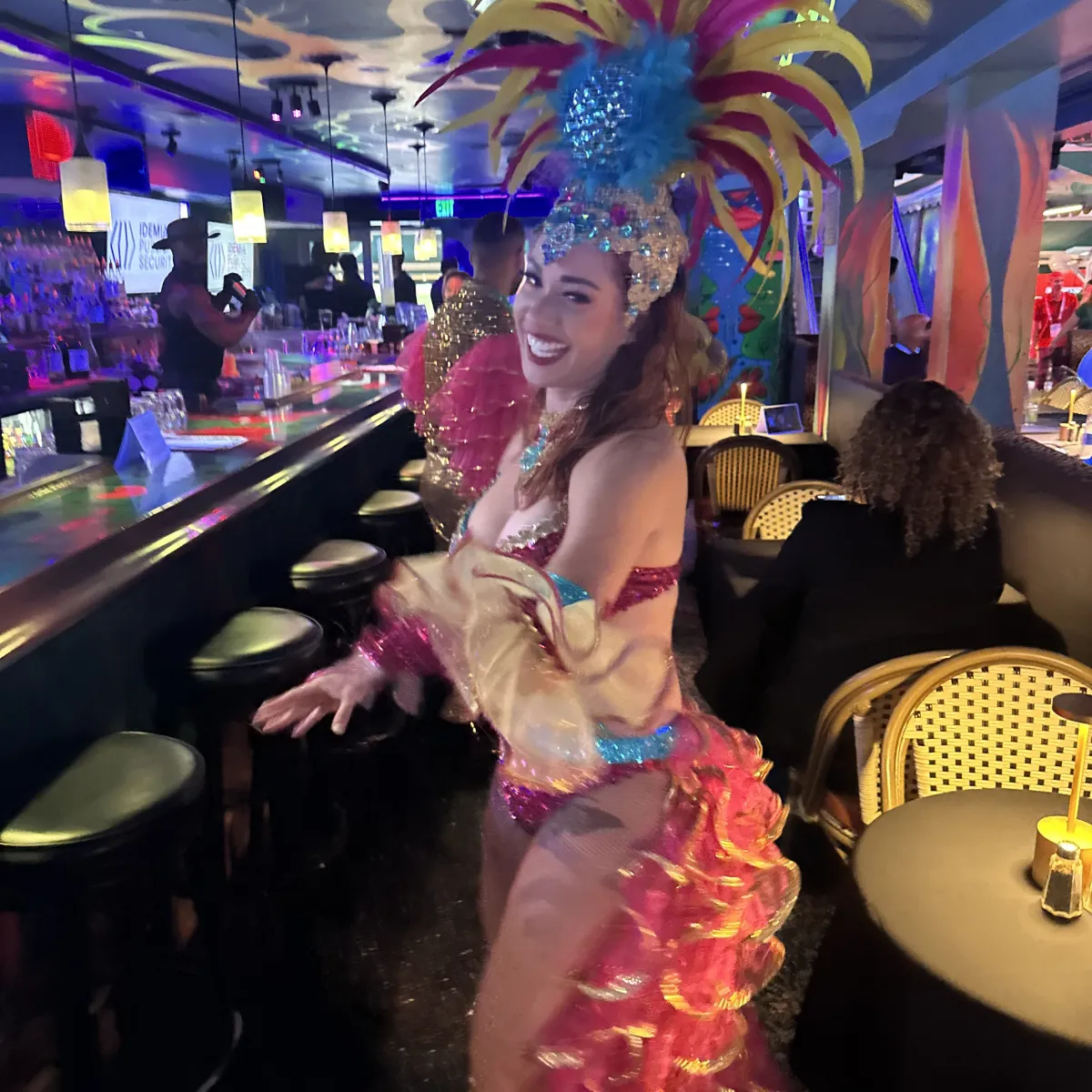 Colorfully dressed dancer with large headdress in lively bar setting. Miami Sip Savor Salsa Lessons Mojitos Live Music Dancing Nightclub Party Nightlife Experience